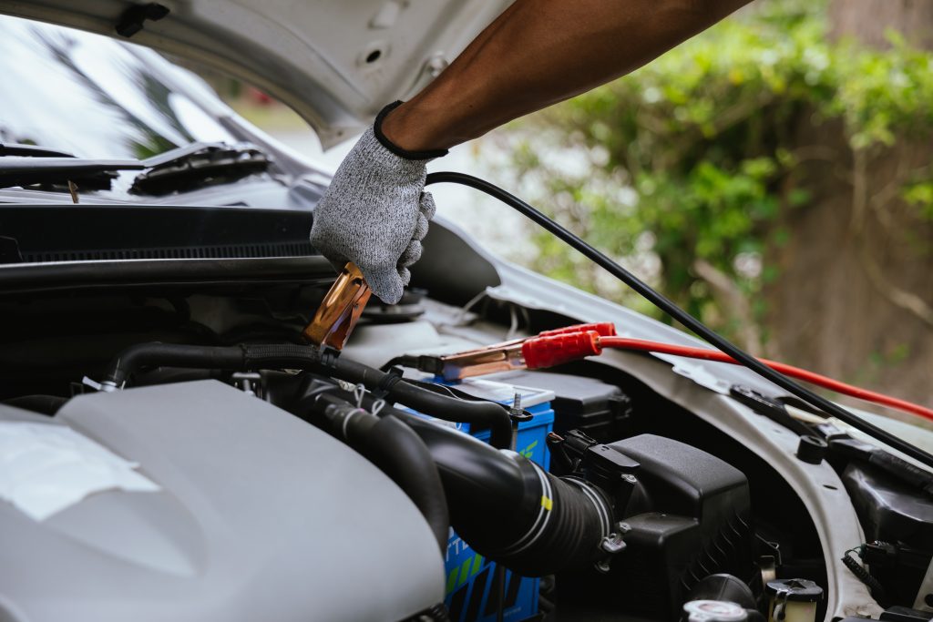 Muž v rukaviciach nabíja autobatériu cez štartovacie káble.
